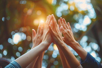A group of people giving a collective high five outdoors, symbolizing unity, teamwork, and celebration of success, with sunlight filtering through the trees