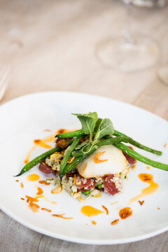 Close-up of black cod fish filet with a Chinese sausage and rice side dish and green beans on a dinner plate, at an event, Canada