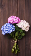 A beautiful bouquet features purple hydrangeas, pink roses, and lavender delphiniums, arranged with green stock flowers and yellow carnations on a rustic wooden table