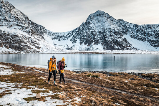 Two women hiking along the shoreline of the frozen Rabbit Lake in Chugach State Park near Anchorage; Anchorage, Alaska, United States of America
