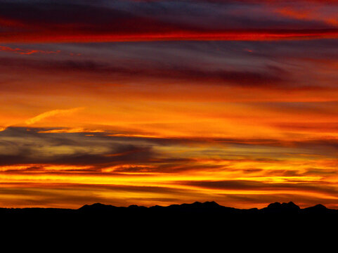 Colorful red and gold clouds in a dramatic sky with a silhouetted mountain range; Calgary, Alberta, Canada