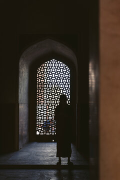 Silhouetted person stands inside Humayun's Tomb looking out to the daylight through a decorative opening; New Delhi, India