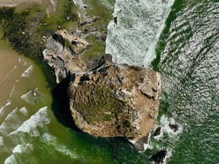 Birds Eye view of the iconic Haystack Rock rising high from the Pacific Ocean amidst the serene beauty of Cannon Beach, where tide pools meet the endless horizon and the Cascade Mountains rise high.