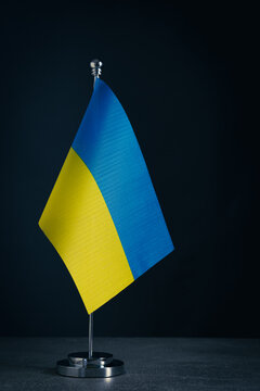 Flag Ukraine on metal table holder dark background. Colors flag are blue and yellow, symbolizing sky and wheat fields.