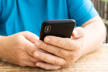 Close-up of male hands holding a mobile phone at a table.