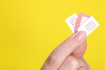 Woman holding SIM cards on yellow background, closeup. Space for text