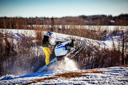 Man enjoys an outing riding his snowmobile and doing jumps while coming out of a valley on a beautiful winter day; Bon Accord, Alberta, Canada