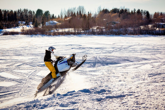 Man enjoys an outing riding his snowmobile and doing jumps while coming out of a valley on a beautiful winter day; Bon Accord, Alberta, Canada