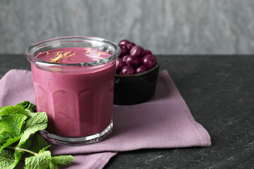 Tasty fresh acai juice in glass with mint and berries on grey textured table, space for text