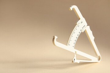 Plastic body fat caliper on beige background. Space for text