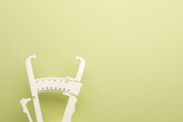 Plastic body fat caliper on light green background. Space for text