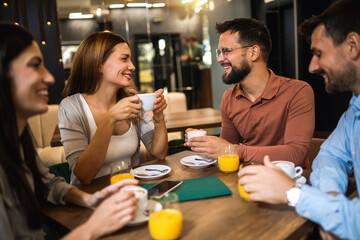 Group of friends met at the cafe. Drinking coffee and orange juice. Girl and guy are talking while the other friends are listening to them.
