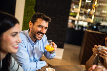 Guy listening to his friends in the cafe while drinking orange juice.