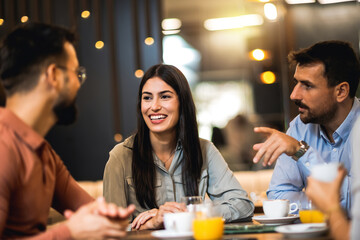 Group of friends hanging out at the cafe. The girl takes the lead in the conversation. Drinking orange juice and coffee.