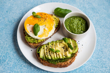 Two toasts with avocado, egg and pesto sauce. A balanced breakfast for a healthy and keto diet.
