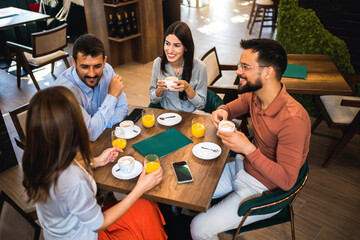 Group of friends laughing together at the coffee shop. They drink orange juice and hang out together.