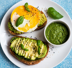 Two toasts with avocado, egg and pesto sauce. A balanced breakfast for a healthy and keto diet.