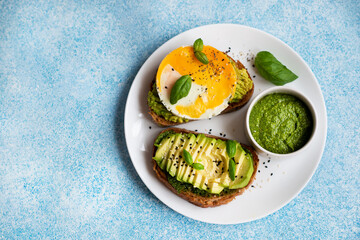 Two toasts with avocado, egg and pesto sauce. A balanced breakfast .
