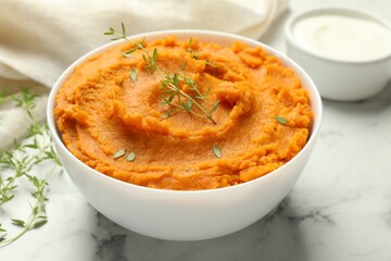 Delicious mashed sweet potatoes in bowl, microgreens and sour cream on white marble table, closeup