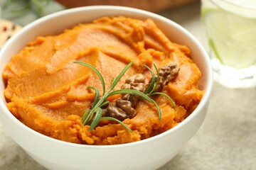 Delicious mashed sweet potatoes with walnuts and rosemary in bowl on light table, closeup