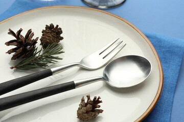 Beautiful Christmas setting with plate, cutlery and cones on blue table, closeup