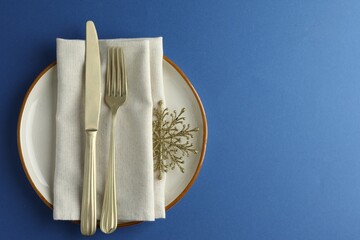 Beautiful Christmas setting with plate, elegant cutlery and golden snowflake on blue table, top...