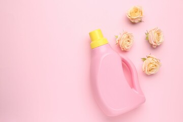 Bottle of laundry detergent and flowers on pink background, closeup. Space for text