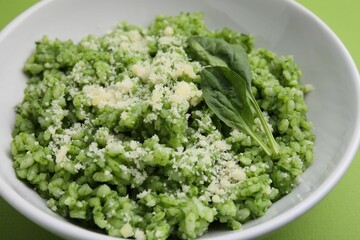 Delicious spinach risotto with parmesan cheese on light green background, closeup