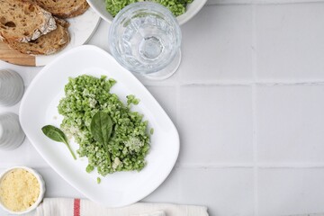 Delicious spinach risotto with parmesan cheese on white tiled table, flat lay. Space for text