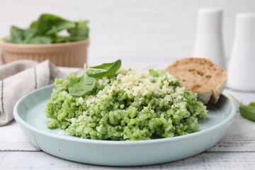 Tasty spinach risotto served with bread on white wooden table, closeup