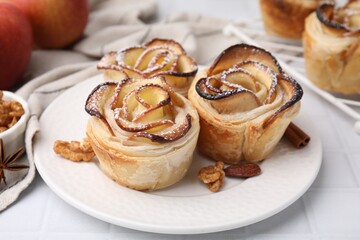 Freshly baked apple roses and walnuts on white tiled table, closeup. Puff pastry