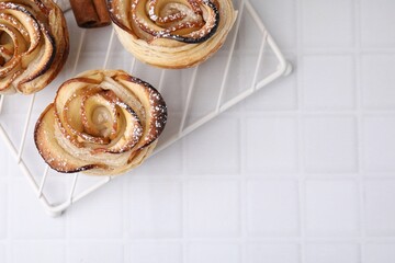 Freshly baked apple roses on white tiled table, top view with space for text. Puff pastry