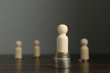 Financial inequality. One wooden figure with bigger stack of coins than others on table