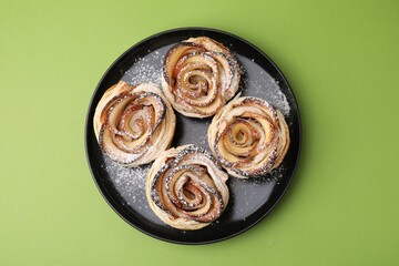 Freshly baked apple roses on green background, top view