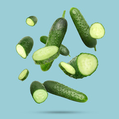 Many ripe cucumbers falling on light blue background