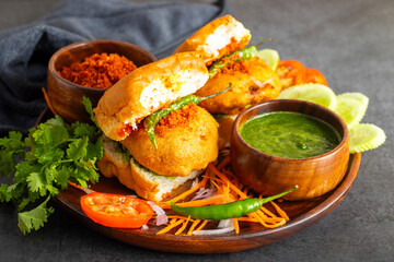 selective focus of Mumbai's famous street food delicious Vada Pav, With coriander leave chutney, tomato sauce, dry garlic chutney and fried chilli. 