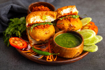 selective focus of Mumbai's famous street food delicious Vada Pav, With coriander leave chutney, tomato sauce, dry garlic chutney and fried chilli. 