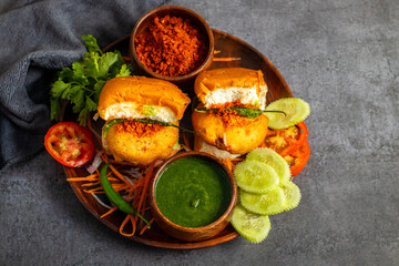 selective focus of Mumbai's famous street food delicious Vada Pav, With coriander leave chutney, tomato sauce, dry garlic chutney and fried chilli. 