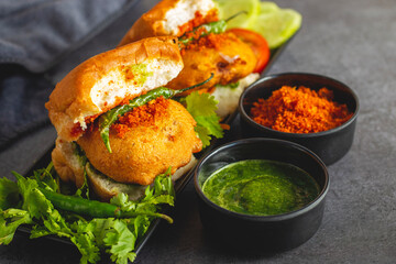 selective focus of Mumbai's famous street food delicious Vada Pav, With coriander leave chutney, tomato sauce, dry garlic chutney and fried chilli. 