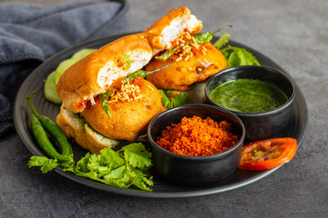 selective focus of Mumbai's famous street food delicious Vada Pav, With coriander leave chutney, tomato sauce, dry garlic chutney and fried chilli. 