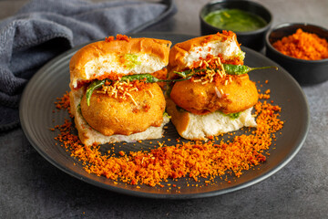 selective focus of Mumbai's famous street food delicious Vada Pav, With coriander leave chutney, tomato sauce, dry garlic chutney and fried chilli. 