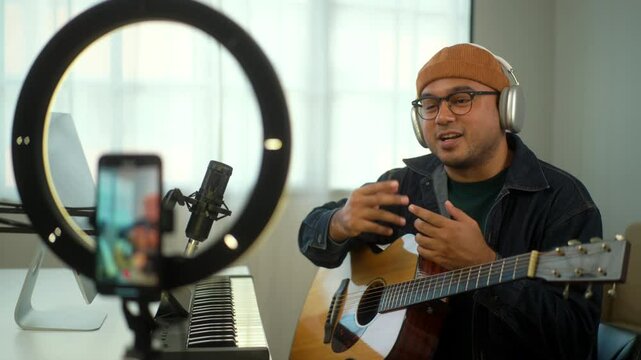 Musician man in headphone teaching guitar online lesson with music instruments and talking to camera in digital recording studio home, a composer blogger man recording music audio video by smartphone.