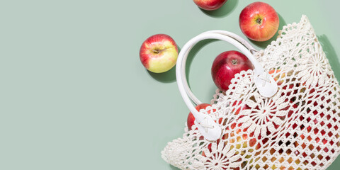 Red apples spilling from crocheted bag on pastel green background, highlighting natural, seasonal fruits. Concept of sustainable living, healthy eating, and mindful consumption. Copy space