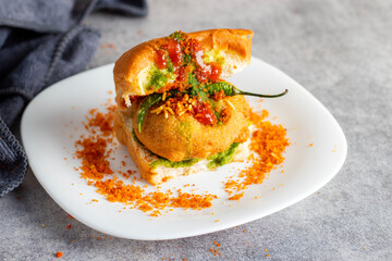 selective focus of Mumbai's famous street food delicious Vada Pav, With coriander leave chutney, tomato sauce, dry garlic chutney and fried chilli. 