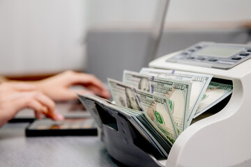 Close-up of hands counting US dollar bills in an automatic cash counter. Ideal for financial, banking, and currency exchange themes. Perfect for promoting financial services and business solutions.