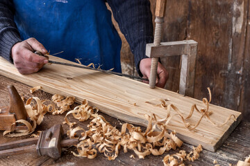 craftsman hand finishes a wooden board clamped with a vice using an old blade and a plane
