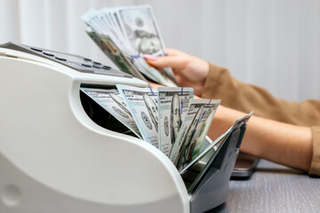 A businesswoman uses a money counter at her desk, with focus on financial management and precision in business operations. Ideal for themes of finance, accounting, and successful entrepreneurship.