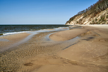 Baltic sea coast with sandy beach and cliff overgrown with trees on Wolin island