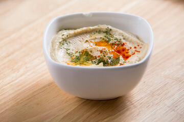Hummus in a small bowl served on a wooden table spiced with paprika powder and olive oil on it middle eastern style