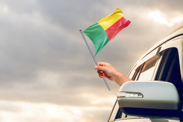 Waving the Benin flag against the sunrise or sunset from a car driving along a country road....